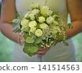 Bride holds a bouquet of white flowers at an outdoor wedding ceremony 141514563