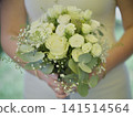 Bridal bouquet with white flowers and green leaves held by a person 141514564