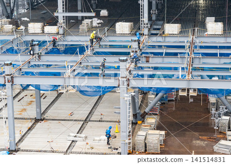 Two workers installing steel frames that were brought in by crane at a construction site in the rain. Two workers installing steel frames that were brought in by crane at a construction site in the rain. 141514831