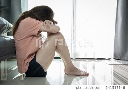 Depressed woman sitting alone in living room caused of sadness or broken heart. Depression is a form of highly negative thinking towards oneself, others and life. Depressed woman sitting alone in living room caused of sadness or broken heart. Depression is a form of highly negative thinking towards oneself, others and life. 141515146