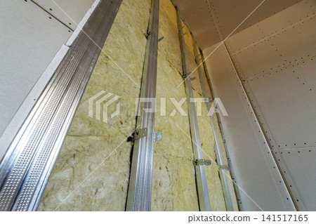 Wall of a room under renovation with mineral rock wool insulation and metal frame prepared for drywall plates. Wall of a room under renovation with mineral rock wool insulation and metal frame prepared for drywall plates. 141517165