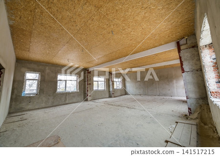 Unfinished apartment or house big loft room under reconstruction. Plywood ceiling, plastered walls, window openings, cement floor. Construction and renovation concept. Unfinished apartment or house big loft room under reconstruction. Plywood ceiling, plastered walls, window openings, cement floor. Construction and renovation concept. 141517215