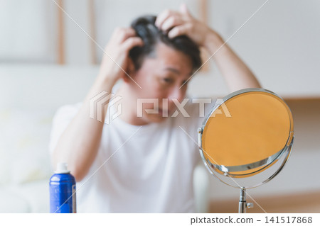 一位四十多歲的男子在桌面鏡子前按摩頭皮。 一位四十多歲的男子在桌面鏡子前按摩頭皮。 141517868