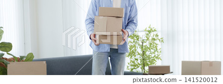 Asian man holding stacked cardboard boxes in bright living room during house move with copy space Asian man holding stacked cardboard boxes in bright living room during house move with copy space 141520012