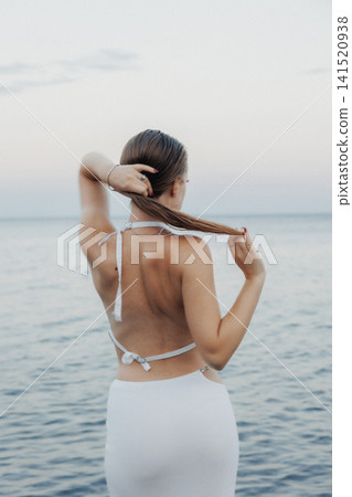 Woman stands ocean's edge, back to camera Woman stands ocean's edge, back to camera 141520938