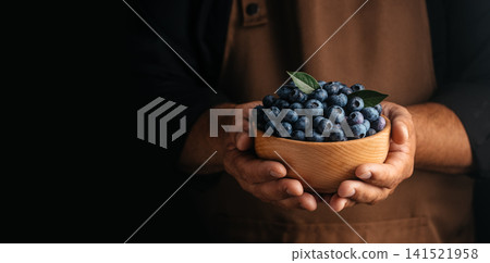 Fresh Blueberries in Wooden Bowl Held by Hands on Dark Rustic Background. Copy Space 141521958
