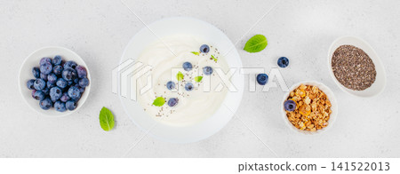 Healthy yogurt with blueberries chia granola and mint on white background top view Healthy yogurt with blueberries chia granola and mint on white background top view 141522013