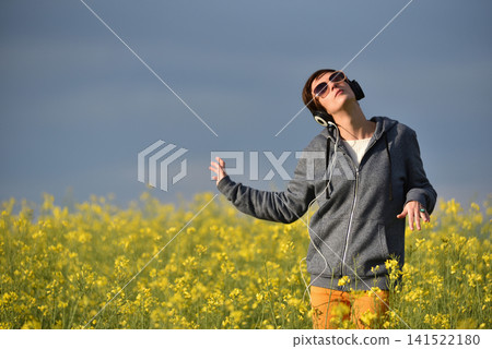 Woman with headphones listening to music in a yellow canola flower field Woman with headphones listening to music in a yellow canola flower field 141522180