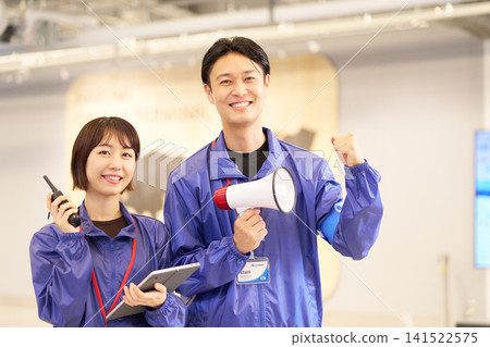 A male and female staff member at the event venue smiles, holding a megaphone and a walkie-talkie. A male and female staff member at the event venue smiles, holding a megaphone and a walkie-talkie. 141522575