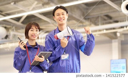 A male and female event staff member, holding a megaphone and a walkie-talkie, smiles and makes a triumphant gesture. A male and female event staff member, holding a megaphone and a walkie-talkie, smiles and makes a triumphant gesture. 141522577