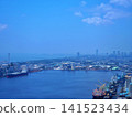 A harbor scene under a blue sky, with cargo ships, shipbuilding facilities, and a panoramic view of the coastal industrial area. 141523434