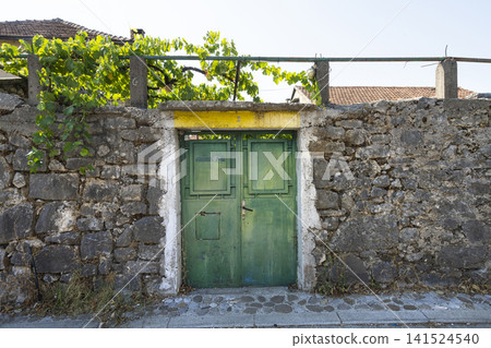A weathered stone wall surrounds a pair of old green double doors. in Podgorica, Montenegro A weathered stone wall surrounds a pair of old green double doors. in Podgorica, Montenegro 141524540