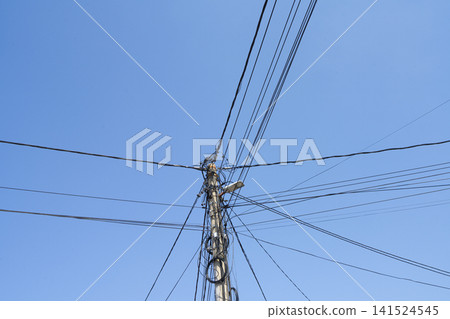 A telephone pole with many wires is silhouetted against a bright, sunlit blue sky. A telephone pole with many wires is silhouetted against a bright, sunlit blue sky. 141524545