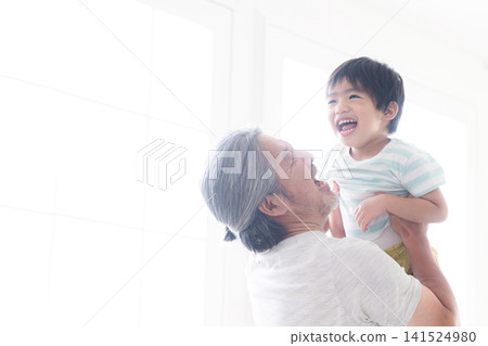 A gray-haired grandfather plays with his child, tossing him high in the air and holding him in his arms, against the backlight. This image evokes feelings of interaction with grandchildren, childcare, and parenting. A gray-haired grandfather plays with his child, tossing him high in the air and holding him in his arms, against the backlight. This image evokes feelings of interaction with grandchildren, childcare, and parenting. 141524980