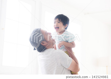 A gray-haired grandfather plays with his child, tossing him high in the air and holding him in his arms, against the backlight. This image evokes feelings of interaction with grandchildren, childcare, and parenting. A gray-haired grandfather plays with his child, tossing him high in the air and holding him in his arms, against the backlight. This image evokes feelings of interaction with grandchildren, childcare, and parenting. 141524981
