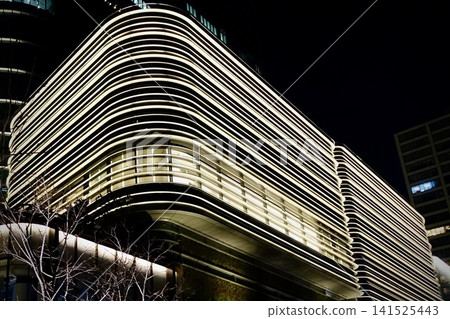 The beautifully undulating exterior design of Azabudai Hills, illuminated at night, and the cityscape in Minato Ward, Tokyo. The beautifully undulating exterior design of Azabudai Hills, illuminated at night, and the cityscape in Minato Ward, Tokyo. 141525443