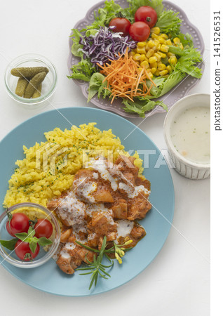 A lunch set featuring butter chicken curry and colorful vegetables served on a blue plate. 141526531