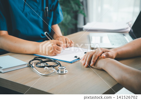 Doctor writing medical notes while comforting a patient during clinic consultation, healthcare support, patient care, trust, diagnosis, and medical service concept. Doctor writing medical notes while comforting a patient during clinic consultation, healthcare support, patient care, trust, diagnosis, and medical service concept. 141526702