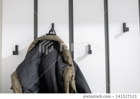 Winter jacket hanging on a black wall hook against white hallway panels, showing everyday outerwear storage, home organization, entryway interior and seasonal clothing at home use 141527123