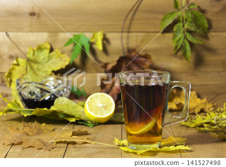 Glass cup of tea, jam and lemon on a background of a wooden surface and yellow leaves 141527498