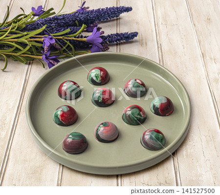 Collectible handmade tempered chocolate sweets with a glossy painted body on a round plate Collectible handmade tempered chocolate sweets with a glossy painted body on a round plate 141527500
