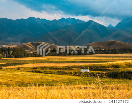 Serene Mountain Landscape with Van in Golden Fields of Kyrgyzstan Serene Mountain Landscape with Van in Golden Fields of Kyrgyzstan 141527572