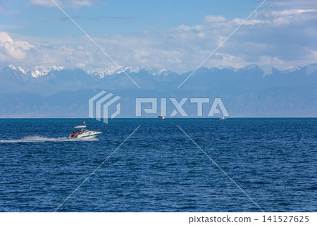 Speedboat with people on Issyk-Kul lake against snow-capped mountains in Kyrgyzstan Speedboat with people on Issyk-Kul lake against snow-capped mountains in Kyrgyzstan 141527625