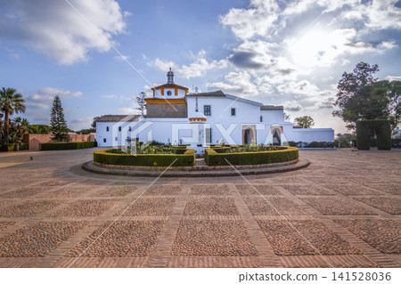 La Rabida Monastery in Huelva Andalusia Spain. Historic Franciscan friary complex with courtyard garden cobblestone square and traditional white building under blue sky. La Rabida Monastery in Huelva Andalusia Spain. Historic Franciscan friary complex with courtyard garden cobblestone square and traditional white building under blue sky. 141528036