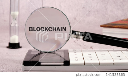 Detailed view of the word Blockchain being magnified on a desk setting next to an hourglass and some books to represent financial technology analysis Detailed view of the word Blockchain being magnified on a desk setting next to an hourglass and some books to represent financial technology analysis 141528863