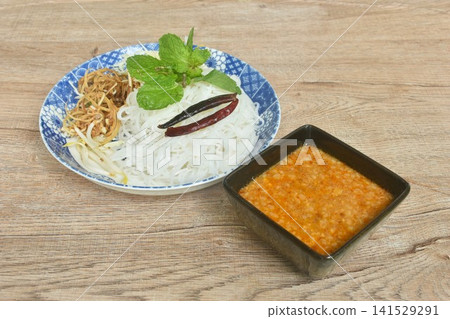rice noodles topping fried chili and fresh vegetable on plate with sweet coconut milk mashed bean curry sauce in bowl rice noodles topping fried chili and fresh vegetable on plate with sweet coconut milk mashed bean curry sauce in bowl 141529291