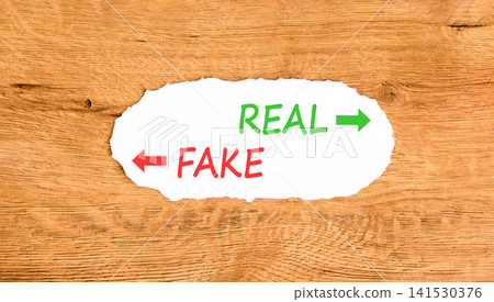 Real or fake words symbol. Concept words Fake and Real on beautiful white paper. Beautiful wooden background. Business and real or fake concept. Copy space. Real or fake words symbol. Concept words Fake and Real on beautiful white paper. Beautiful wooden background. Business and real or fake concept. Copy space. 141530376