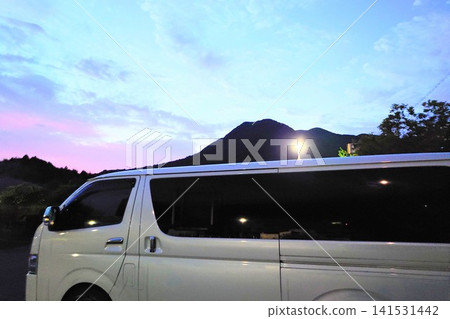 A white minivan and a mountain landscape as morning (or evening) arrives after an overnight stay in the car. A white minivan and a mountain landscape as morning (or evening) arrives after an overnight stay in the car. 141531442