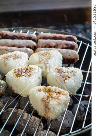 A barbecue in the bright sunshine: sausages and grilled rice balls placed on a round barbecue grill. A barbecue in the bright sunshine: sausages and grilled rice balls placed on a round barbecue grill. 141531656