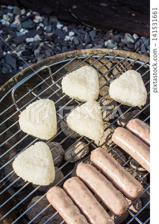 A barbecue in the bright sunshine: sausages and grilled rice balls placed on a round barbecue grill. A barbecue in the bright sunshine: sausages and grilled rice balls placed on a round barbecue grill. 141531661