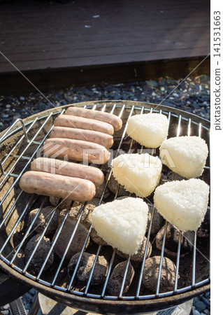A barbecue in the bright sunshine: sausages and grilled rice balls placed on a round barbecue grill. A barbecue in the bright sunshine: sausages and grilled rice balls placed on a round barbecue grill. 141531663