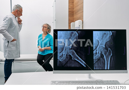Experienced orthopedist discussing pelvic bone X-ray with elderly female patient. Diagnostics of hip joint osteoarthritis and fracture. Experienced orthopedist discussing pelvic bone X-ray with elderly female patient. Diagnostics of hip joint osteoarthritis and fracture. 141531703