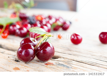 Shiny cherries with leaf on rustic wooden table, close view with soft blur, bright natural light, glossy red fruit texture and fresh summer harvest mood, with berry, summer, juicy, background detail Shiny cherries with leaf on rustic wooden table, close view with soft blur, bright natural light, glossy red fruit texture and fresh summer harvest mood, with berry, summer, juicy, background detail 141531917
