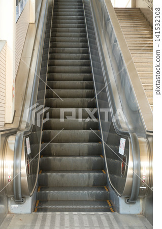 The symmetrical composition captures the straight lines of an unmanned escalator at a train station, along with an emergency stop button and safety warning sticker. The symmetrical composition captures the straight lines of an unmanned escalator at a train station, along with an emergency stop button and safety warning sticker. 141532108