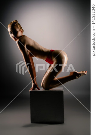 Woman posing on black cube in red underwear with dramatic studio lighting Woman posing on black cube in red underwear with dramatic studio lighting 141532340