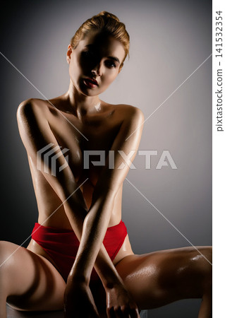 Woman in red bikini with glossy skin under dramatic studio lighting 141532354
