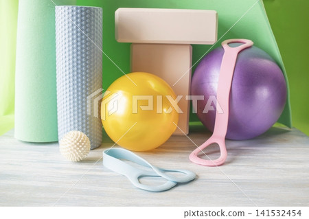 Fitness and yoga equipment in the gym. Exercise tools. Fitness equipment with yoga mat, blocks, expander and balls on a wooden surface. Fitness and yoga equipment in the gym. Exercise tools. Fitness equipment with yoga mat, blocks, expander and balls on a wooden surface. 141532454