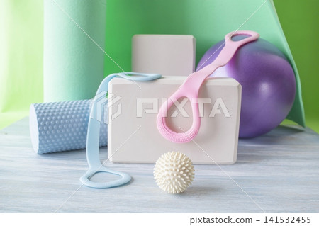 Fitness and yoga equipment in the gym. Exercise tools. Fitness equipment with yoga mat, blocks, expander and balls on a wooden surface. Fitness and yoga equipment in the gym. Exercise tools. Fitness equipment with yoga mat, blocks, expander and balls on a wooden surface. 141532455