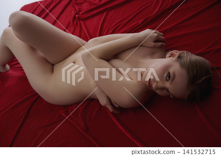 Sensual young woman lying nude on rich red fabric, looking at camera Sensual young woman lying nude on rich red fabric, looking at camera 141532715
