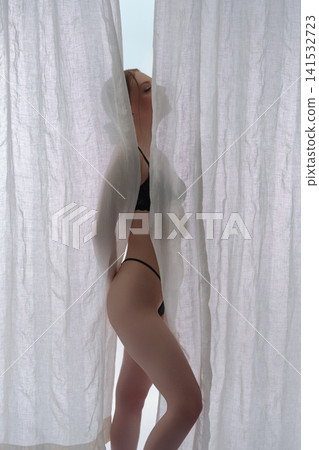 Elegant nude woman from back standing between white sheer curtains Elegant nude woman from back standing between white sheer curtains 141532723