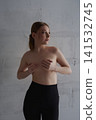 Serene young woman posing topless against minimalist concrete wall 141532745