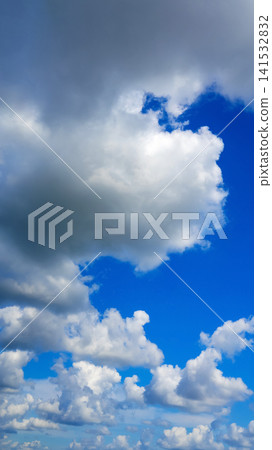 a large darkening cumulus cloud above white clouds in a bright blue sky 141532832