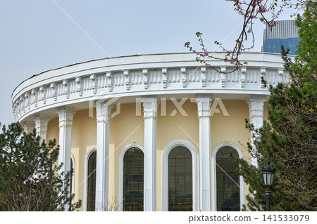 Neoclassical building with white columns and arch windows. Architecture landmark surrounded by garden trees. Urban travel destination and classic city government office exterior design. 141533079