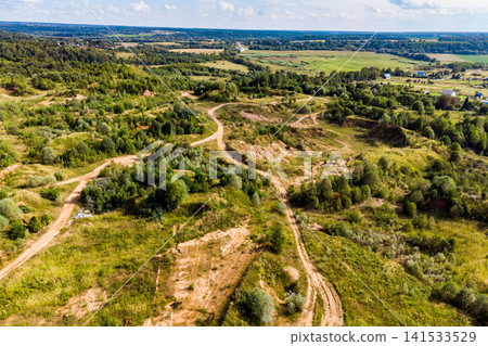 Aerial view of an abandoned sand quarry with winding dirt paths overgrown with lush green bushes and trees, capturing the rugged beauty of a reclaimed industrial terrain 141533529