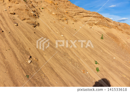 Steep sandy slopes of an industrial quarry featuring textured golden layers and small scattered pebbles under a bright blue sky, capturing raw earthy geology in a natural mining setting Steep sandy slopes of an industrial quarry featuring textured golden layers and small scattered pebbles under a bright blue sky, capturing raw earthy geology in a natural mining setting 141533618