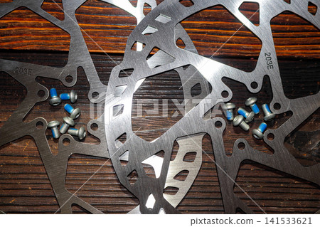Brand new oversized 203mm bicycle brake rotors made of stainless steel with matching mounting screws featuring blue threadlocker applied on wooden background for mechanical repair shop 141533621